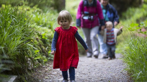 A little girl running ahead of her family along a woodland path at Bodnant Garden, Conwy, Wales